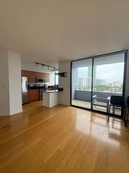 Open living area with wood flooring, a compact kitchen and glass balcony doors.