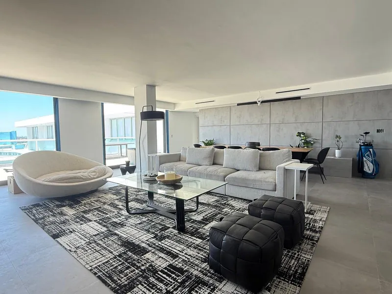 Living room with a cream sofa, round chair, glass coffee table and balcony windows.