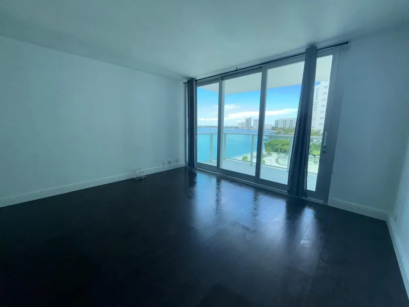 Empty room with dark wood flooring and glass balcony doors overlooking the water.