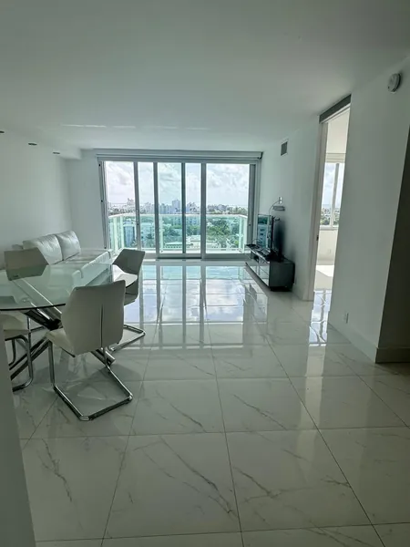 Living and dining area with white furniture, a glass dining table and glossy marble flooring.