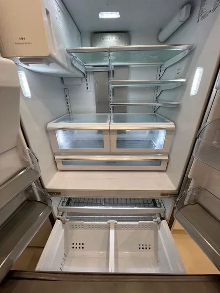 Open, empty refrigerator with glass shelves and pull-out drawers.