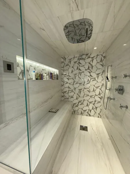 Marble shower with a rainfall showerhead, built-in bench and patterned accent wall.