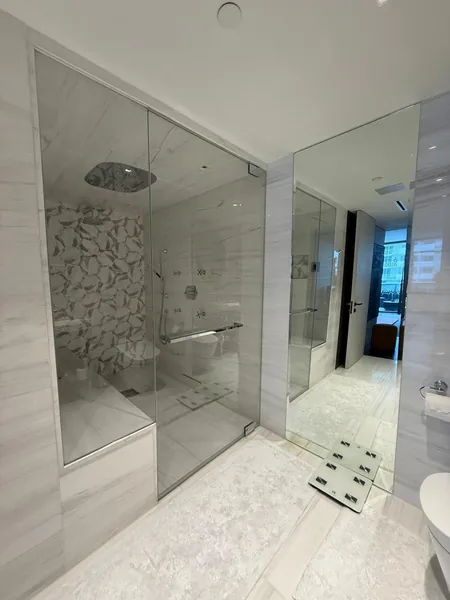 Marble bathroom with a glass shower enclosure, full-length mirror and bath mat.