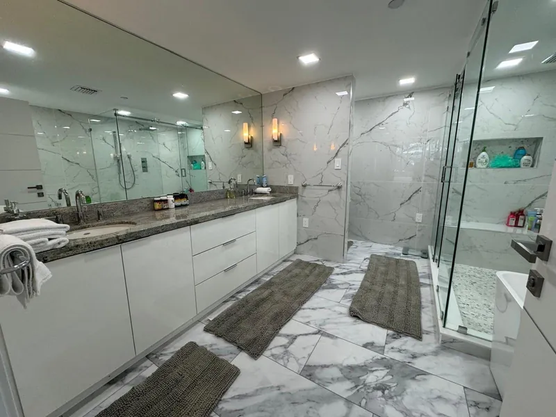 Marble bathroom with a double vanity, wide mirror and glass shower enclosure.